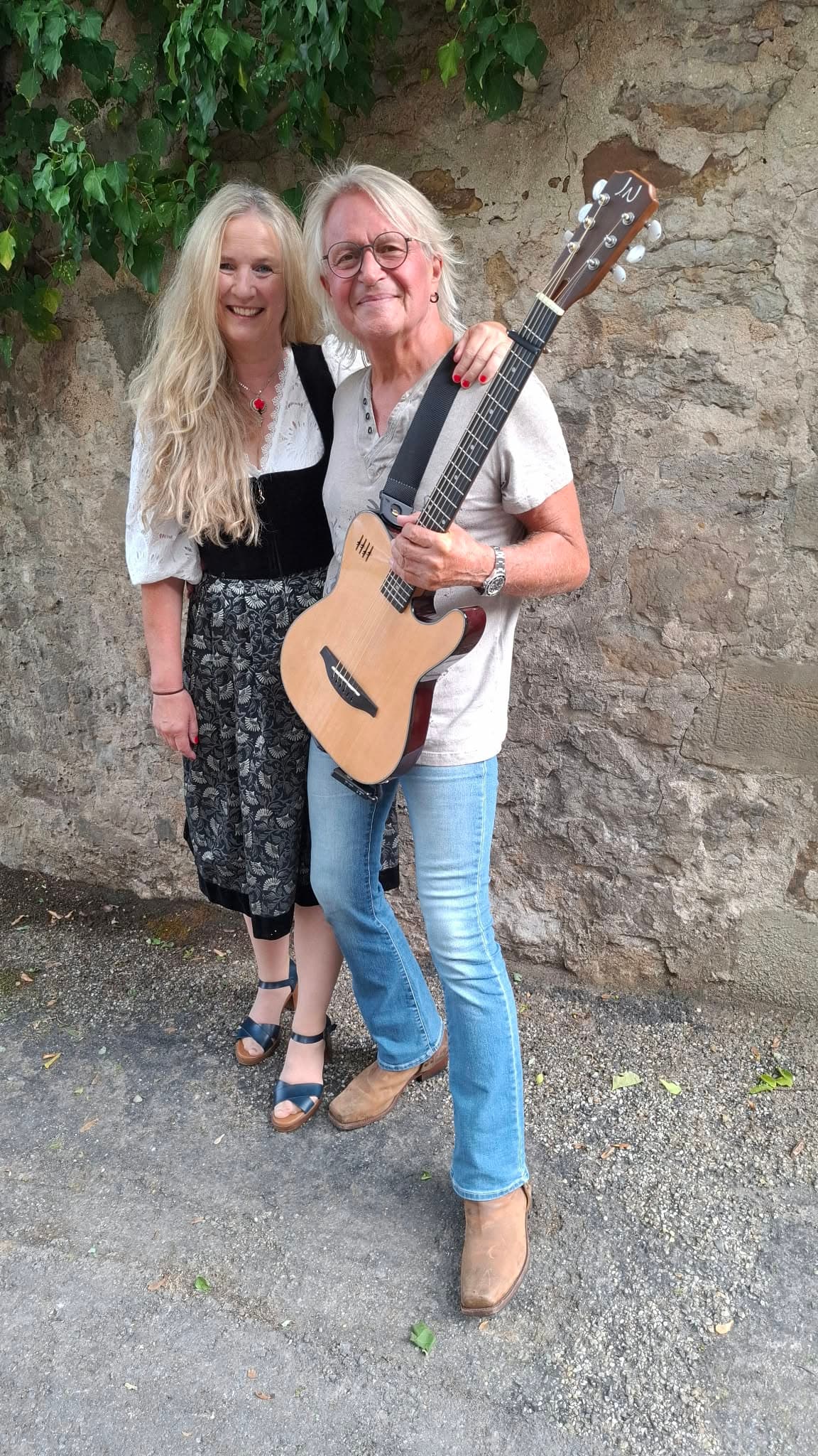 Conny Bains und Richy Vogl mit Gitarre vor einer Steinmauer